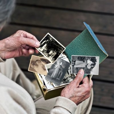 Elderly woman holding old photographs. Adobe.